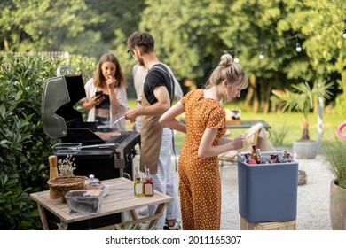 Happy Friends Hang Out On A Picnic, Grilling Food And Standing With Alcohol Drinks At Backyard On Nature. Small Group Of People Cooking And Spending Summertime Outdoors