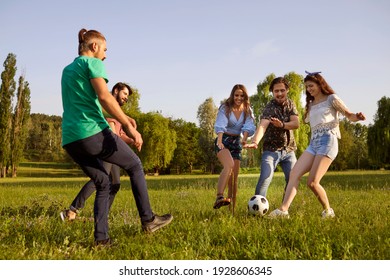 Happy Friends Have Fun Playing Active Games In The Park. Cheerful Young People Playing Soccer On Green Meadow. Group Friends Engaged In Sports Game, Having Fun And Laughing Outdoors On Summer Day