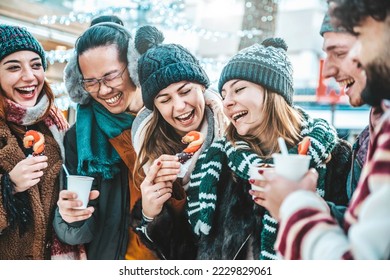 Happy friends having fun drinking mulled wine and hot chocolate at Christmas Market - Cheerful young people enjoying winter holidays on weekend vacation - Focus on asian guy