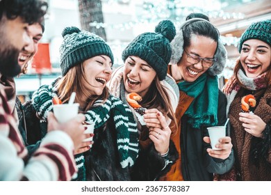 Happy friends having fun drinking mulled wine and hot chocolate at Christmas Market - Cheerful young people enjoying winter holidays on weekend vacation - Tourism lifestyle and friendship concept - Powered by Shutterstock