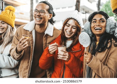 Happy friends having fun drinking mulled wine and hot chocolate at Christmas Market - Young people wearing winter clothes walking in city street  - Powered by Shutterstock