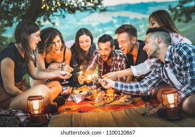 Happy friends having fun with fire sparkles - Young people millennials camping at picnic after sunset - Vacationers enjoying wine at summer barbecue party - Youth friendship concept on night mood