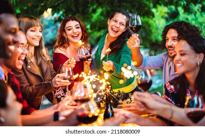 Happy friends having fun with fire sparkles while toasting red wine - Young millenial people camping at summer picnic barbecue party on night mood - Youth life style concept on warm vivid filter - Powered by Shutterstock