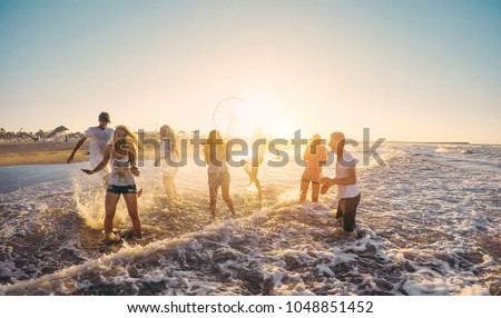 Happy friends having fun on the beach at sunset - Young people playing inside sea water outdoor in summer vacation - Friendship, youth,travel concept - Soft focus on right guys