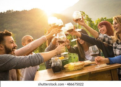 Happy friends having fun outdoor - Young people enjoying harvest time together outside at farm house vineyard countryside - Youth friendship concept - Hands toasting red wine glass at winery on sunset