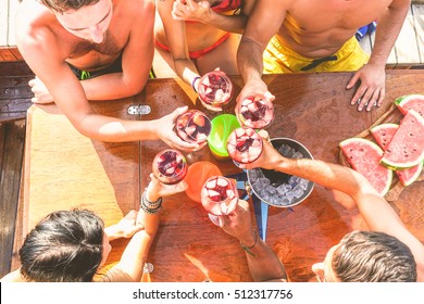 Happy friends having fun outdoors in boat party - Young people enjoying summer vacation together toasting wine with fruit - Youth and friendship concept - Main focus on top hand red wine glass
