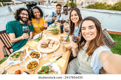 Happy friends having fun at rooftop dinner party - Group of young people taking selfie photo at outdoors dining table - Life style concept with guys and girls eating food and drinking wine together - Powered by Shutterstock