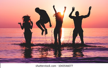 Happy friends jumping inside water on tropical beach at sunset - Group of young people having fun on summer vacation - Youth lifestyle, party and friendship concept - Focus on bodies silhouette - Powered by Shutterstock