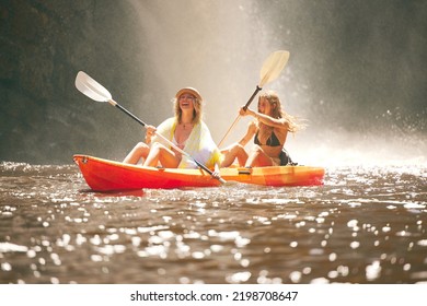 Happy friends kayak on the lake or river together during summer vacation. Free, freedom and rowing women canoeing on a boat and having fun in nature with water activity on weekend at a waterfall