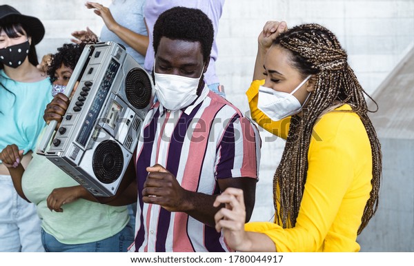 Happy friends listening music with vintage\
boombox and dancing while wearing face mask outdoor - Multiracial\
young people having fun during corona virus outbreak - Youth\
millennial friendship\
concept