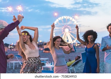 Happy Friends Making Beach Party After Sunset With Fireworks And Drinking Champagne - Young People Having Fun Dancing Outdoor  - Soft Focus On Center Girl Face - Youth And Festival Concept