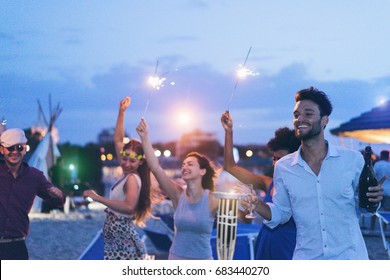 Happy friends making evening beach party outdoor with fireworks and drinking champagne - Young people having fun at chiringuito bar with dj set - Focus on right man face - Youth and summer concept - Powered by Shutterstock