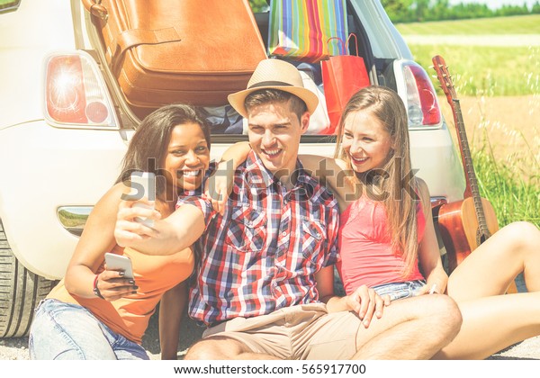Happy friends making selfie photo standing next car full\
of suitcases and bags - Young people having fun in road trip\
holidays - Traveling and friendship holidays concept - Warm\
cinematic filter 