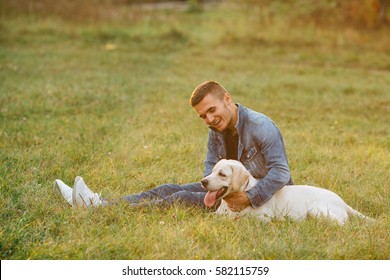 Happy Friends Man And Dog Labrador Sitting On Grass In Park At Sunset. Toned Photo 