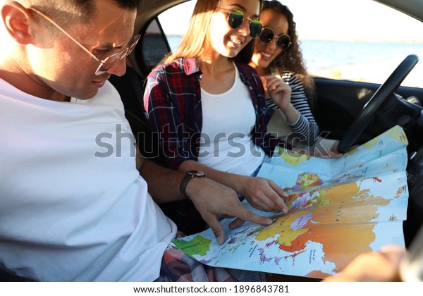 Happy\
friends with map in car on road trip,\
closeup