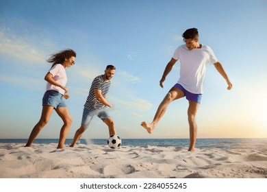 Happy friends playing football on beach during sunset, low angle view - Powered by Shutterstock