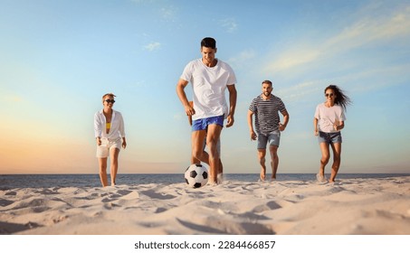 Happy friends playing football on beach during sunset, low angle view - Powered by Shutterstock