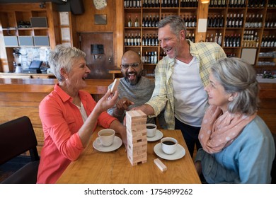 Happy friends playing jenga game while having cup of coffee in bar - Powered by Shutterstock