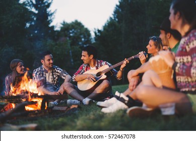 Happy friends playing music and enjoying bonfire in nature