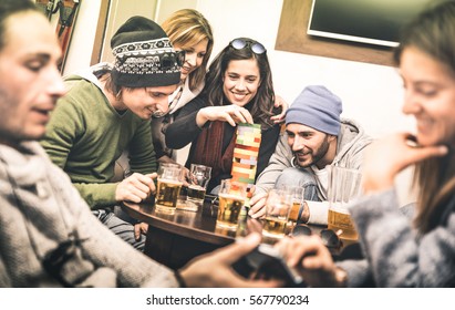 Happy friends playing table board game while drinking beer at pub - Cheerful people having fun at brewery bar corner - Friendship concept on contrast desaturated filter with soft greenery color tones