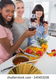 Happy Friends Preparing A Meal Together And Drinking Red Wine At Home In Kitchen