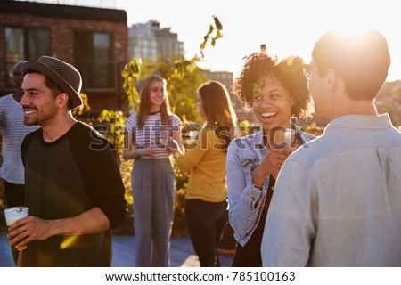 Happy friends at a rooftop party backlit by sunlight
