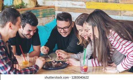 Happy friends sharing slice of cake at restaurant - Friendship concept with young people enjoying time together and having genuine fun at rustic cafe eating chocolate cake - Focus on guy with glasses - Powered by Shutterstock