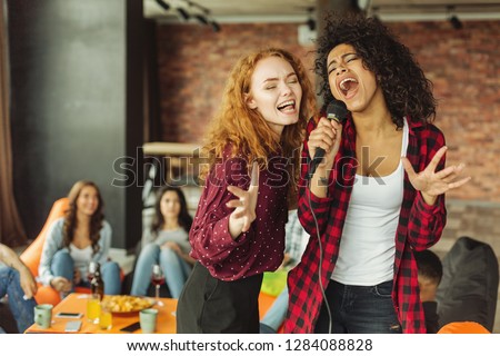 Happy friends singing together at home. Karaoke party concept