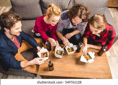 Happy Friends Sitting On Sofa And Eating Noodles With Chopsticks