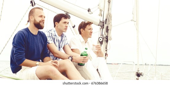 Happy friends sitting together on a deck of a yacht enjoying a good day and having a drink. Summer, holiday concept.