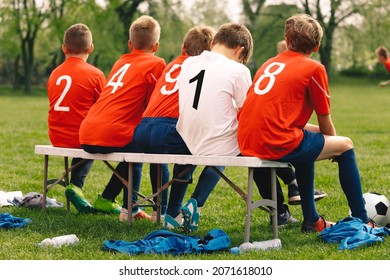 Happy Friends In Sports Team. Group Of Young Boys Kicking Sports Soccer Game On  Grass Pitch. School Boys Sitting On Sideline Substitute Bench. School Kids In Red Sports Jersey Shirts