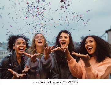 Happy Friends Standing On A Terrace. Group Of Young Women Throwing Confetti.