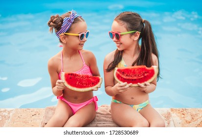 Happy friends in swimwear and sunglasses smiling and looking at each other while sitting near clean pool and enjoying fresh watermelon on resort - Powered by Shutterstock