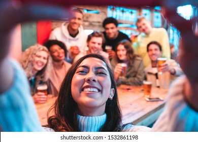 Happy friends taking a group selfie at pub - Group of multiracial millennial people having fun together at pub and taking a photo - Birthday party or after work meeting, happiness and teamwork concept