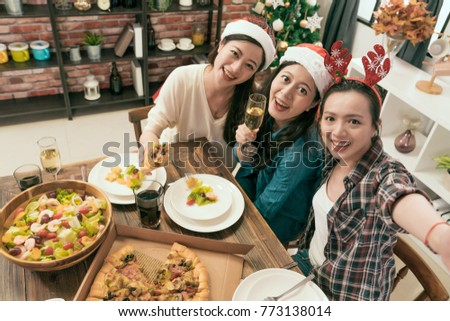 Happy friends taking selfie wearing Santa hats and enjoy drink together in front of the Christmas tree