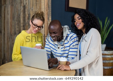 Happy friends using laptop while having coffee in cafÃ©