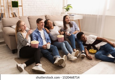 Happy friends watching comedy film at home and eating popcorn on floor - Powered by Shutterstock