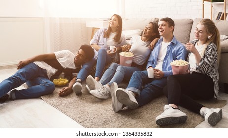 Happy friends watching comedy movie and eating popcorn, sitting on floor at home - Powered by Shutterstock