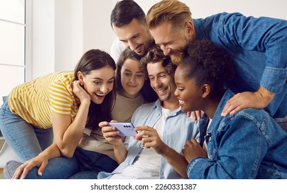 Happy friends watching something on mobile phone and having fun all together. Indoor group shot of cheerful young diverse mixed race people looking at screen of smartphone and enjoying funny videos - Powered by Shutterstock