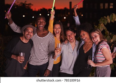 Happy friends waving glowsticks at rooftop party in Brooklyn
