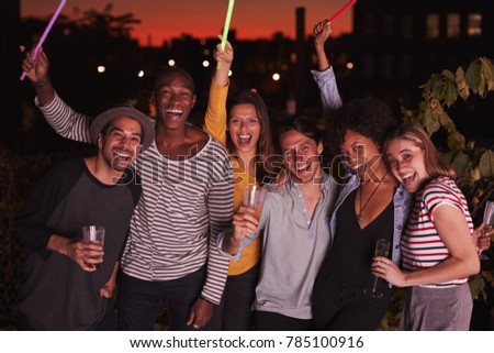 Happy friends waving glowsticks at rooftop party in Brooklyn