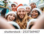 Happy friends wearing santa claus hat taking selfie at Christmas time together on city street - Group of young multi ethnic people having new year party outside - Winter holidays concept