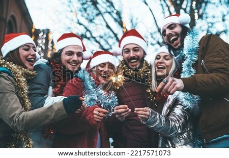 Happy friends wearing santa claus hat celebrating Christmas day holding sparklers - Cheerful young people having new year party outside - Winter traditional holidays concept