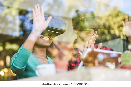 Happy friends wearing virtual reality goggles in modern coworking space - Window reflection view from outside - Smartphones using with vr headset - Focus on african girl mouth glasses - Tech concept - Powered by Shutterstock