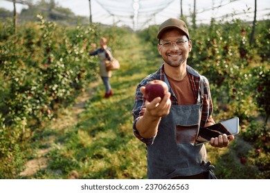 Happy fruit plantation owner using touchpad while harvesting apples and looking at camera.  - Powered by Shutterstock