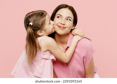Happy fun adorable lovely woman wearing casual clothes with child kid girl 6-7 years old. Daughter kissing mother cheek, look aside isolated on plain pastel pink background. Family parent day concept