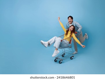 Happy fun Asian woman sitting inside of shopping trolley and man pushing shopping cart to get the latest offers promotion at the supermarket isolated on blue background. - Powered by Shutterstock