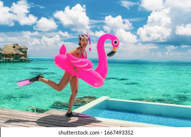 Happy fun beach vacation woman tourist ready to take the plunge jumping in luxury swimming pool at Tahiti resort hotel with snorkel fins and pink flamingo pool float. Funny girl running on holidays.