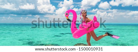 Happy fun beach vacation woman tourist ready to jump in ocean swimming with snorkel fins and pink flamingo toy pool float. Goofy swimmer girl running on holidays panoramic banner.