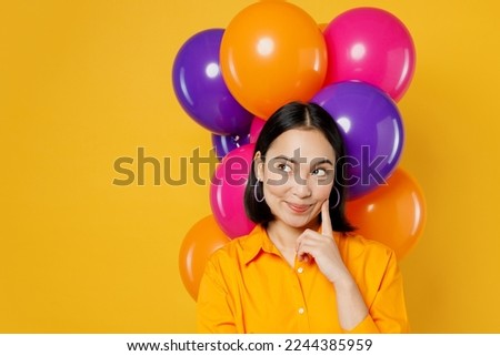 Happy fun dreamful pensive young woman wears casual clothes celebrating near balloons prop up face look aside on area workspace isolated on plain yellow background. Birthday 8 14 holiday party concept